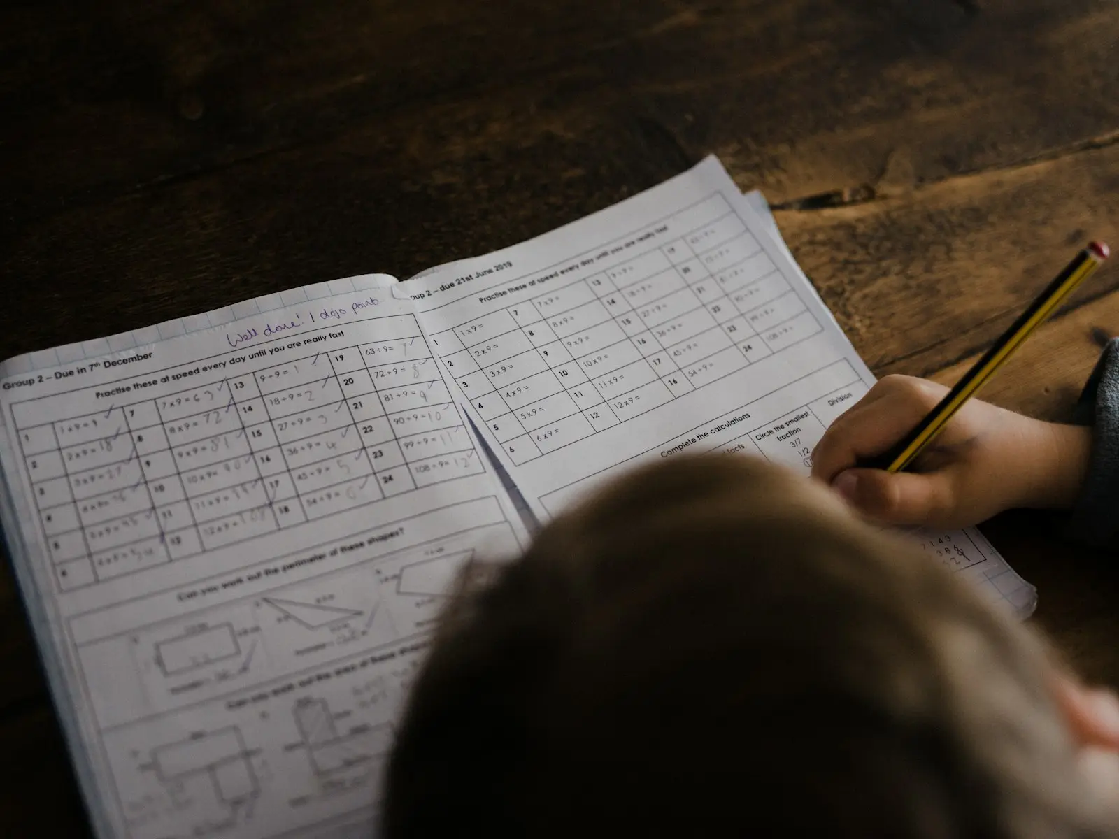 A child works through math problems in an exercise book with a pencil.