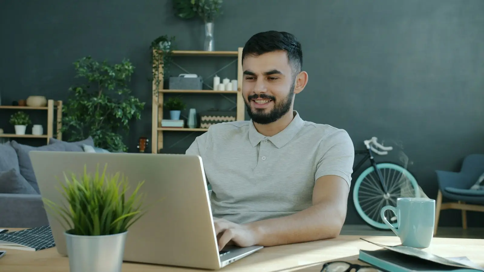 A tutor works at a laptop on a tidy desk with a notebook and a cup of coffee.